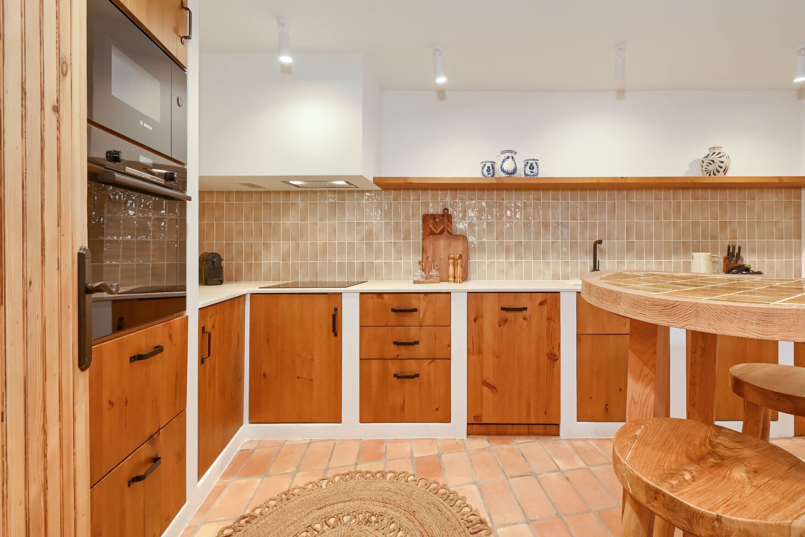A kitchen with wooden cabinets, a built-in oven, a round wooden table, and a woven rug.