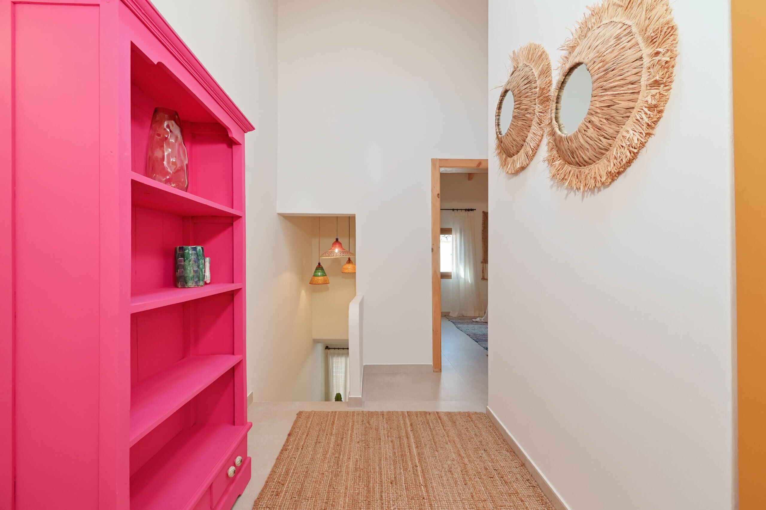Un couloir agrémenté d’une étagère rose vif, d’un tapis tissé et de deux miroirs fixés au mur.