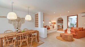 A modern living room with a wooden dining table, wicker chairs, and a sofa with orange cushions. - Casa Paraiso by Marhen Homes (Javea / Xàbia)