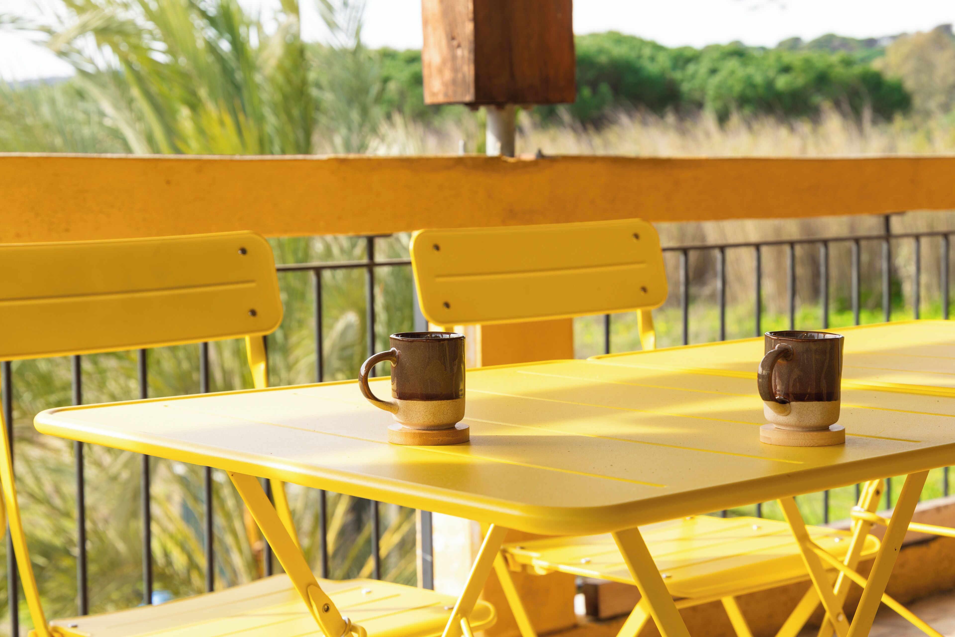 Une table jaune sur laquelle sont posées deux tasses, le tout se détachant sur un fond de verdure.