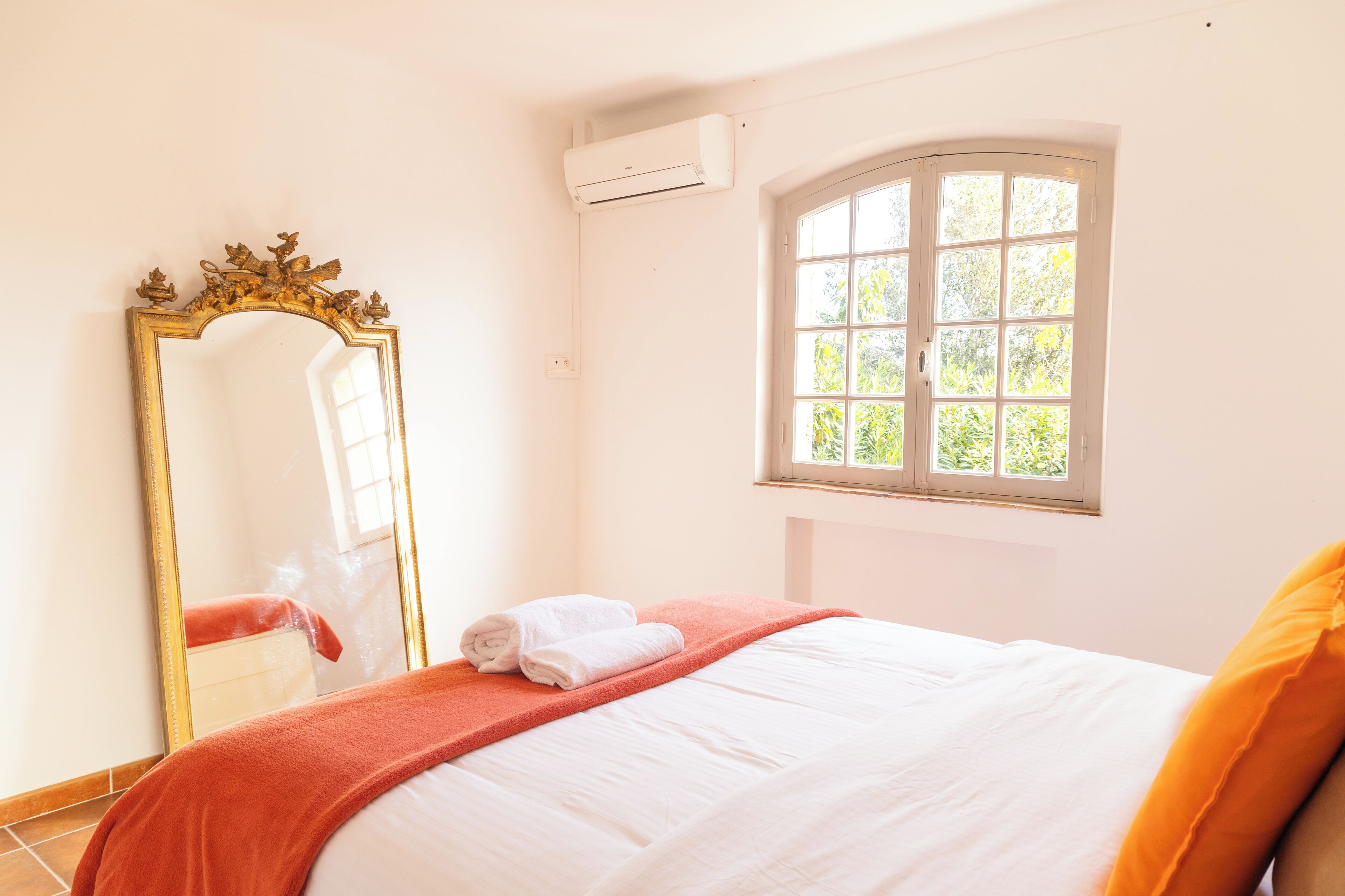 Un dormitorio con cama, un espejo grande, un ventanal y un equipo de aire acondicionado.