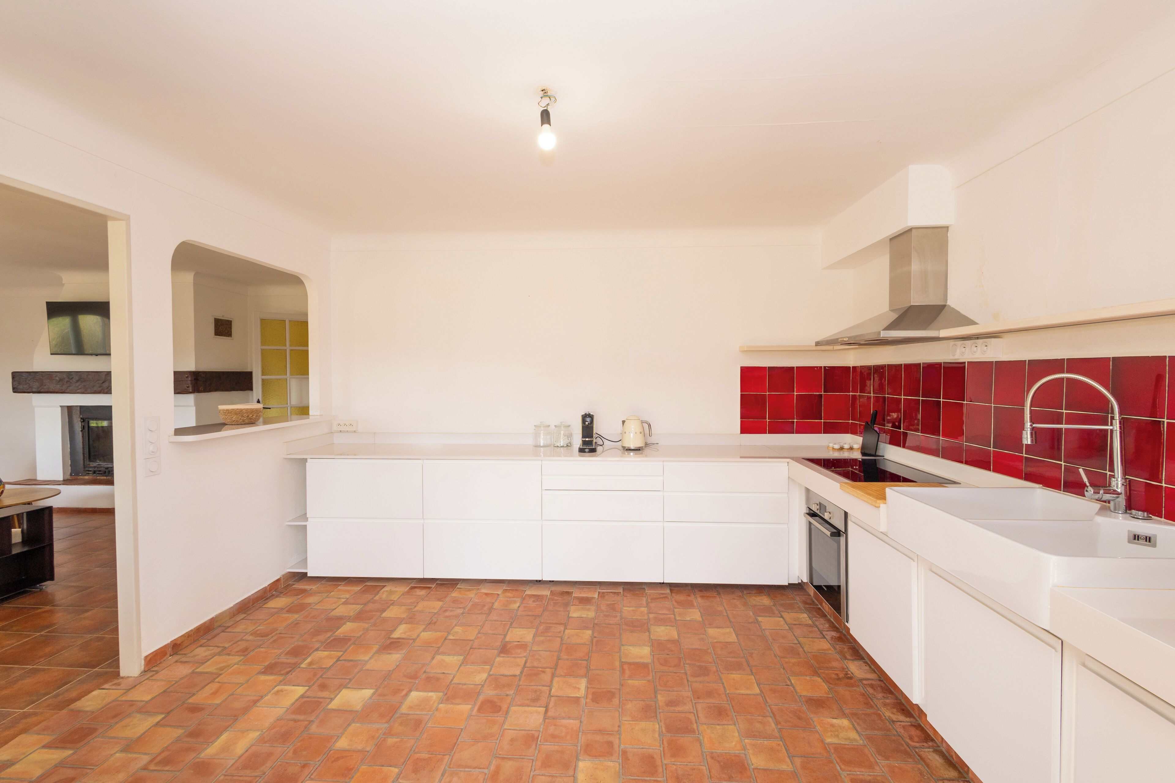 A kitchen with white cabinets, a red backsplash, and a tiled floor.