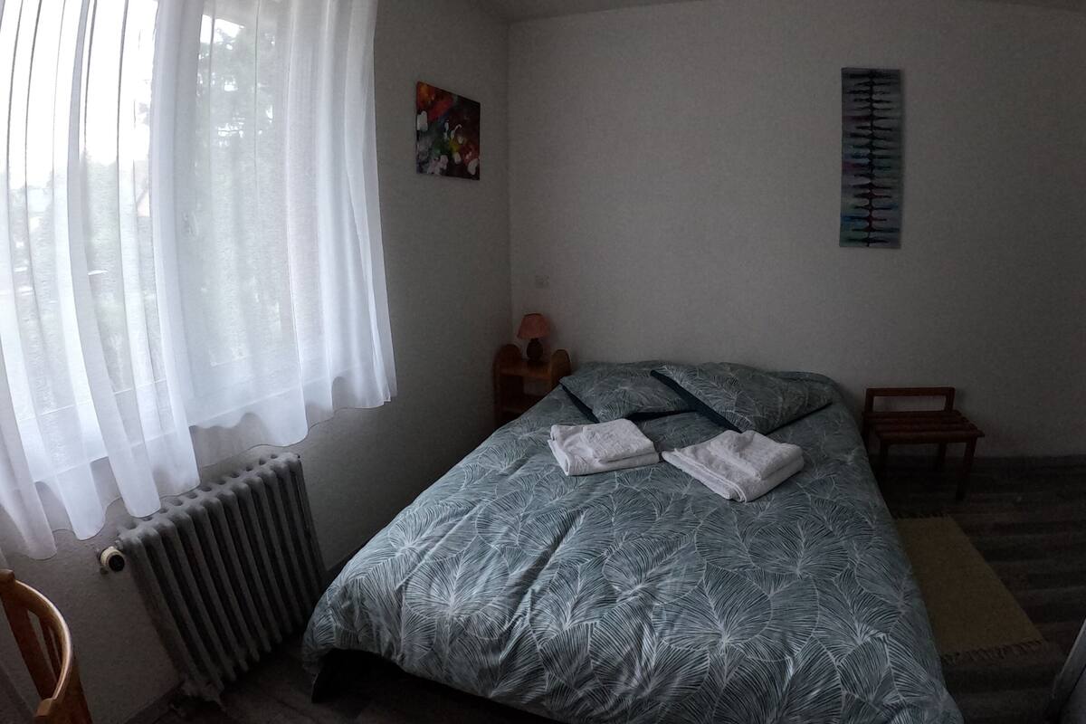 Une chambre à coucher avec un lit, un radiateur, une chaise, une petite table avec une lampe et un mur sur lequel est accroché un calendrier.