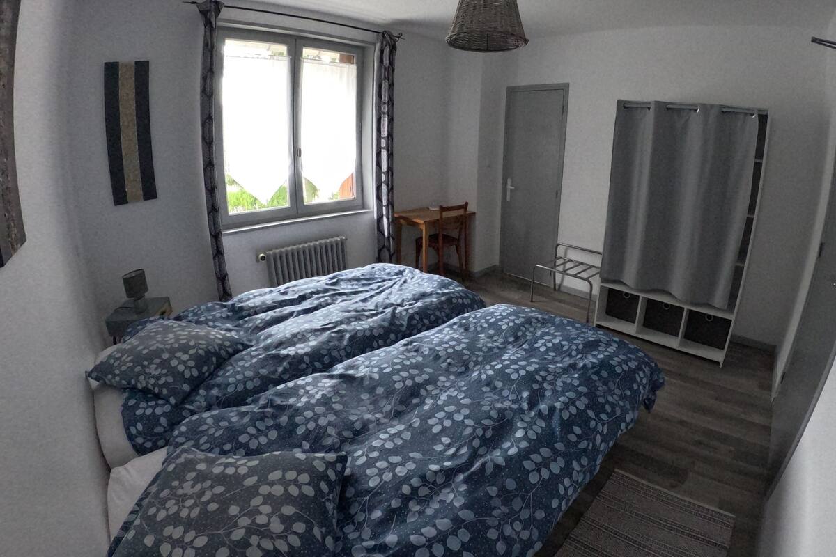 Une chambre à coucher comprenant un lit, une fenêtre, un radiateur, une chaise, une armoire et un luminaire suspendu.