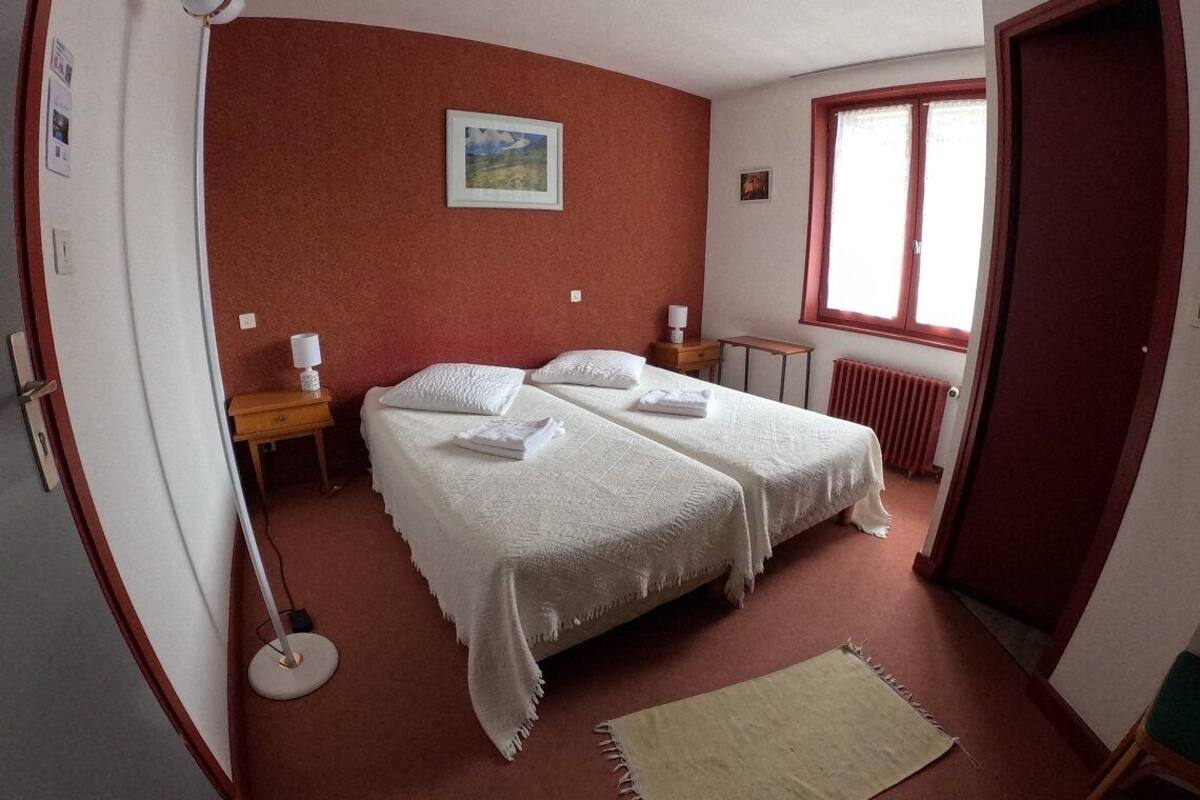 Une chambre avec deux lits, une fenêtre, un radiateur et une petite table avec une lampe.