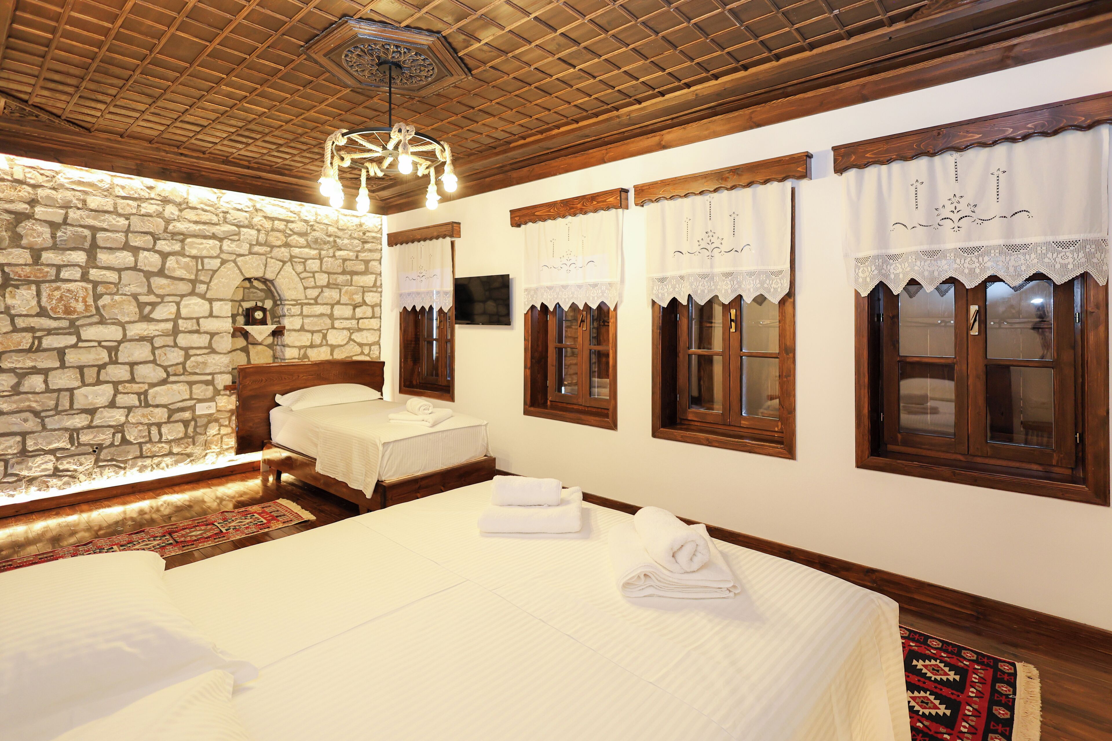 A hotel room with a stone wall, wooden beams, and a large bed with neatly folded towels.