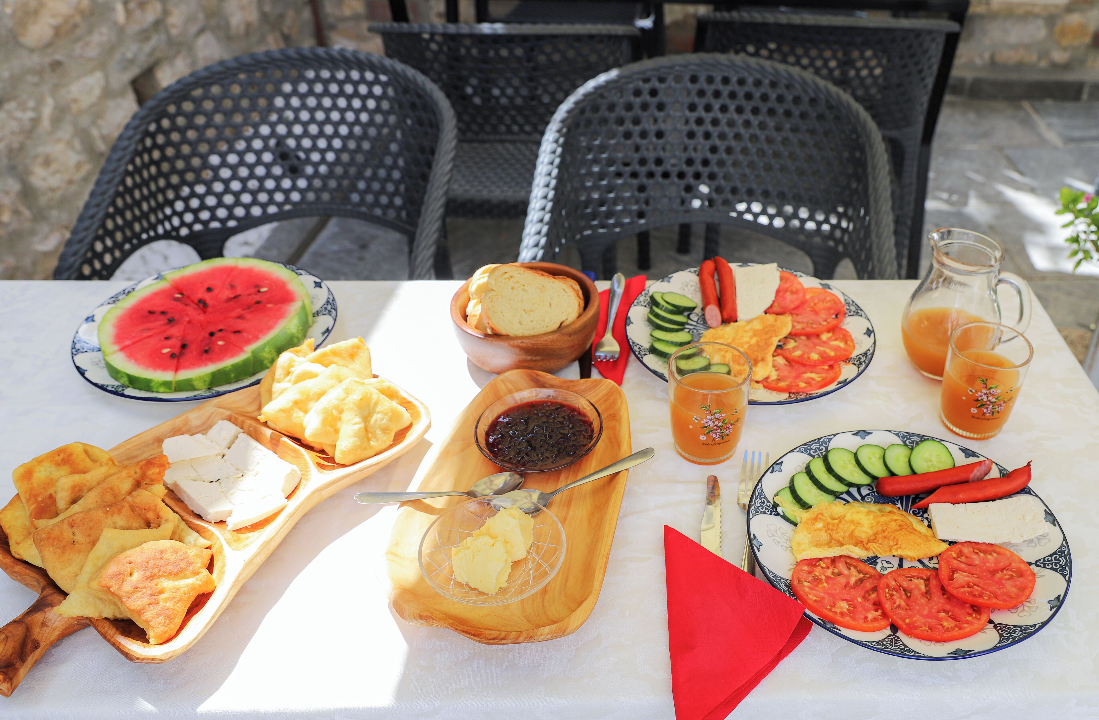 Ein Tisch reichhaltig gedeckt mit verschiedenen Speisen, darunter Brot, Tomaten, Gurken und einem Wassermelonenfächer.