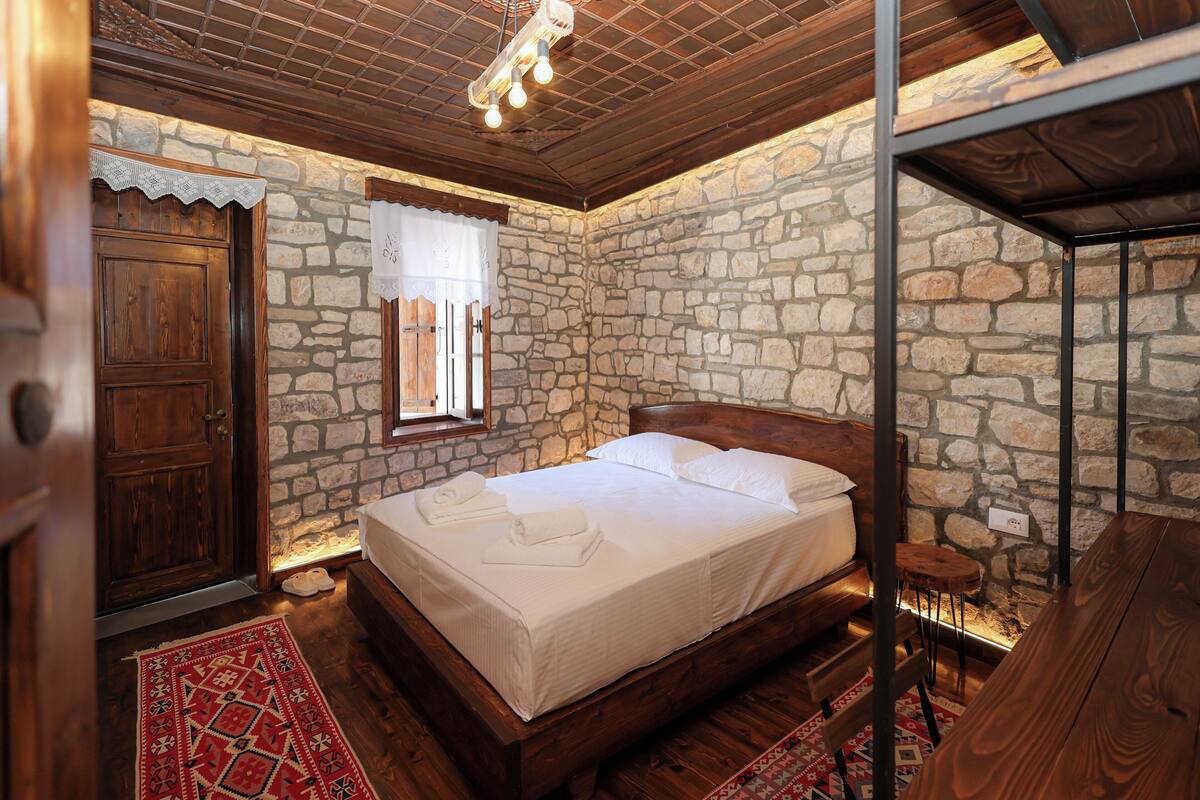 Un dormitorio con pared de piedra, cama de madera y alfombra roja estampada.