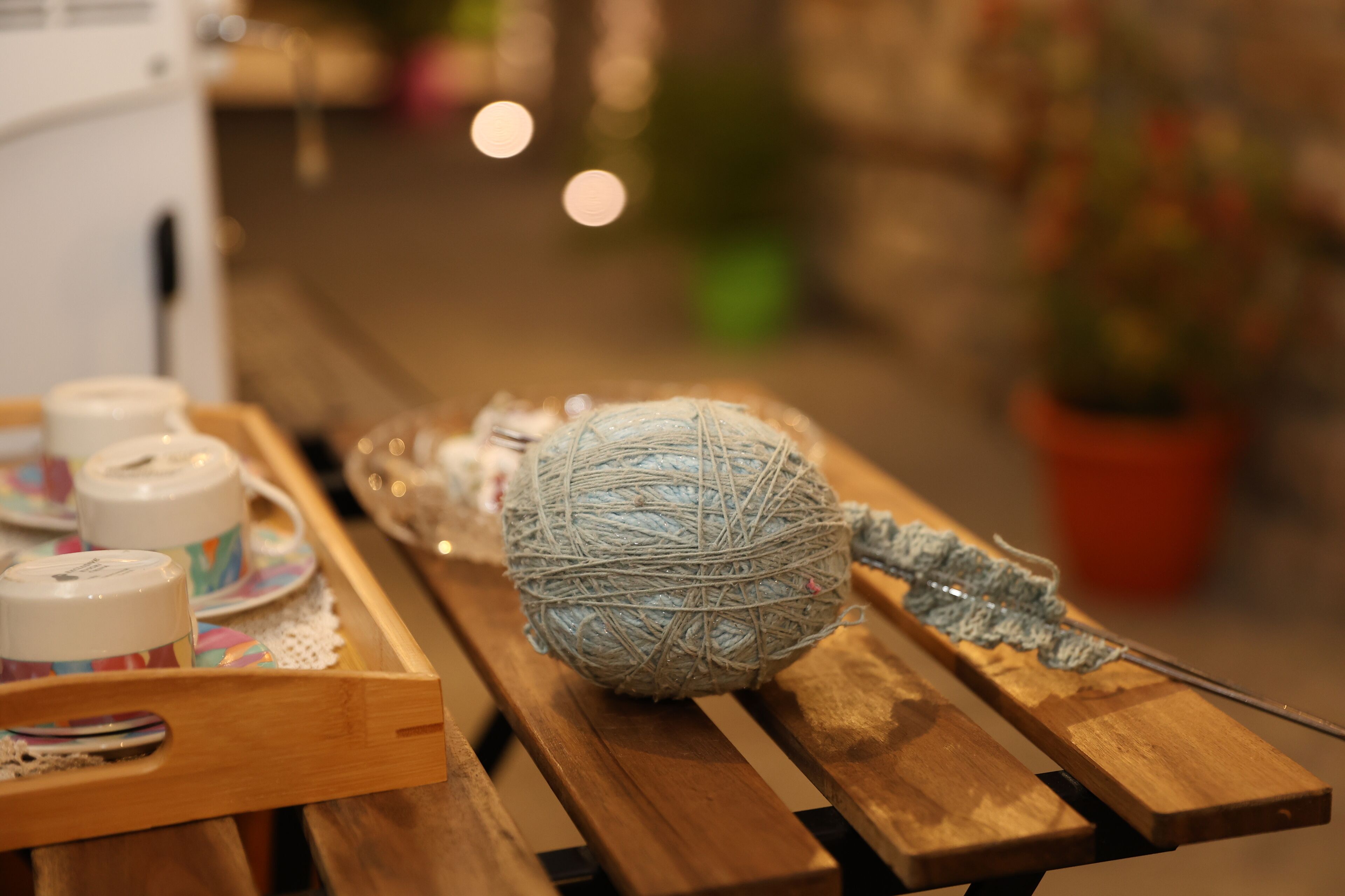 Une table en bois, sur laquelle se trouvent une pelote de laine, un crochet et une napperon en dentelle.