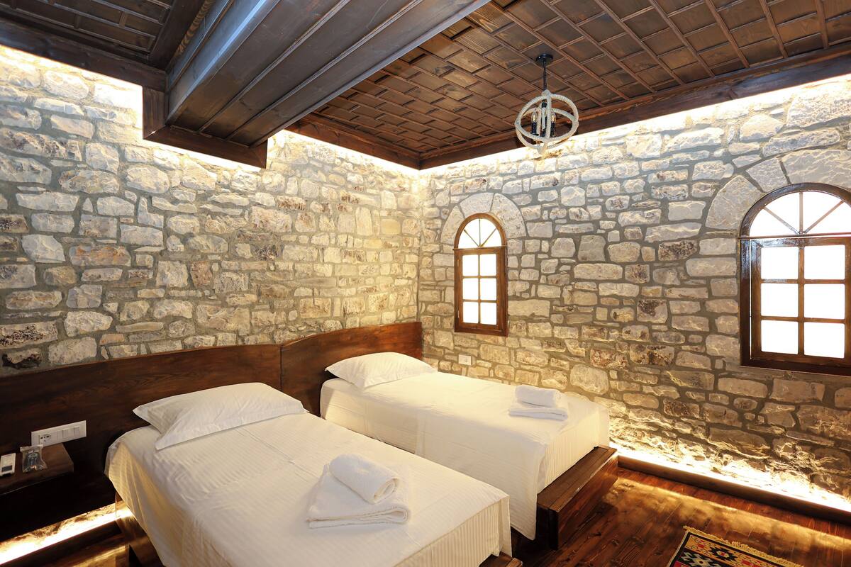 Una habitación con paredes de piedra, vigas de madera y dos camas con ropa blanca.