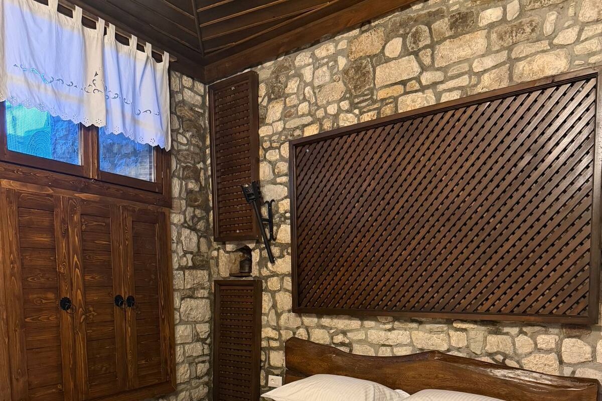 Un dormitorio con cama de madera, pared de piedra y ventana con cortinas.
