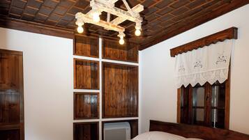 A neatly made bed with white linens and towels, a wooden headboard, and a ceiling with exposed beams and a chandelier.