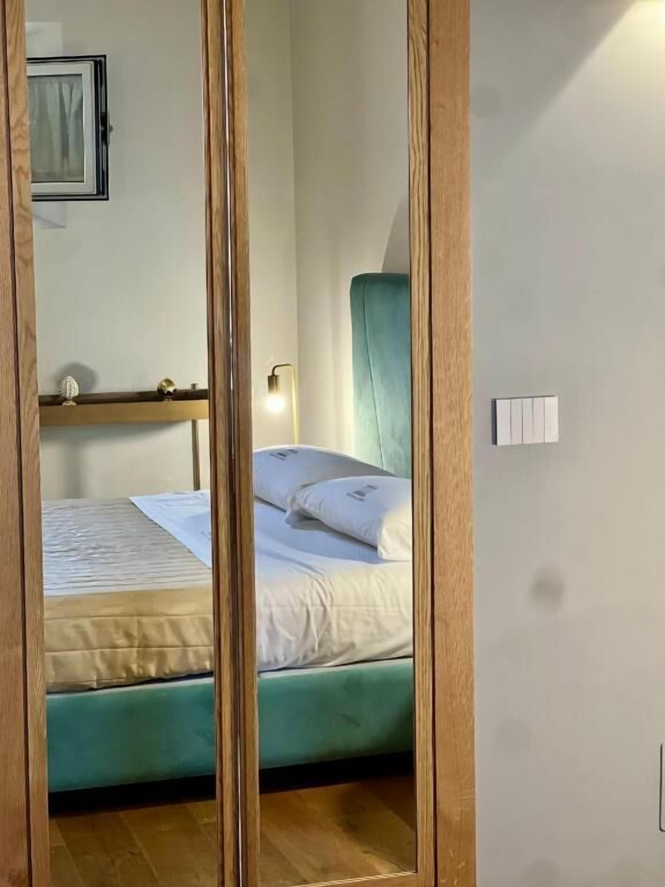 A single bed with a teal headboard, white bedding, and a bedside lamp.