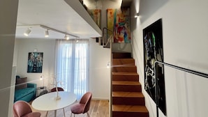 Ein modernes Interieur mit einer Treppe, einem Essbereich mit rosa Stühlen und einem Wohnbereich mit einem blauen Sofa.