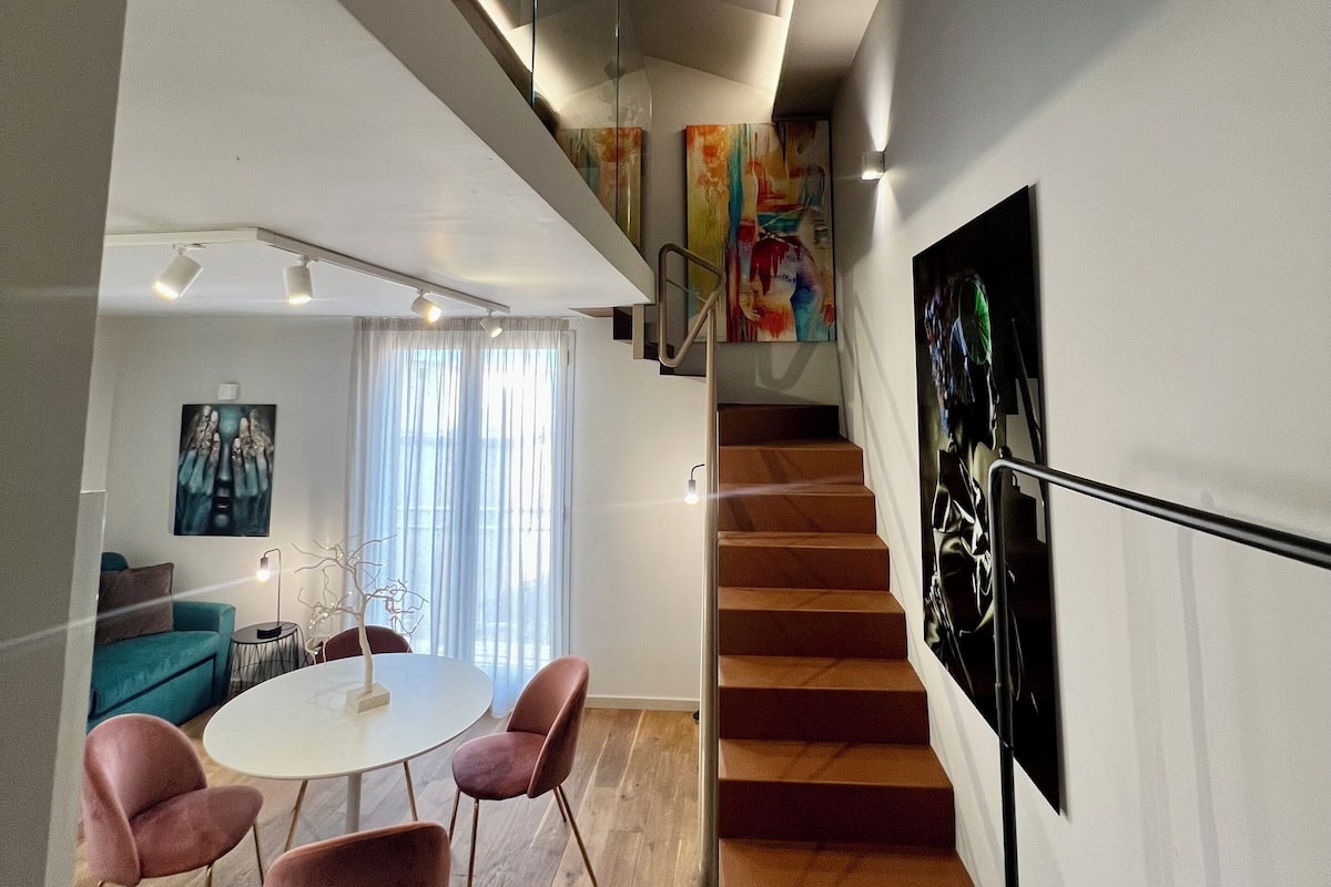 Een modern interieur met een trap, een eetgedeelte met roze stoelen en een zithoek met een blauwe bank.