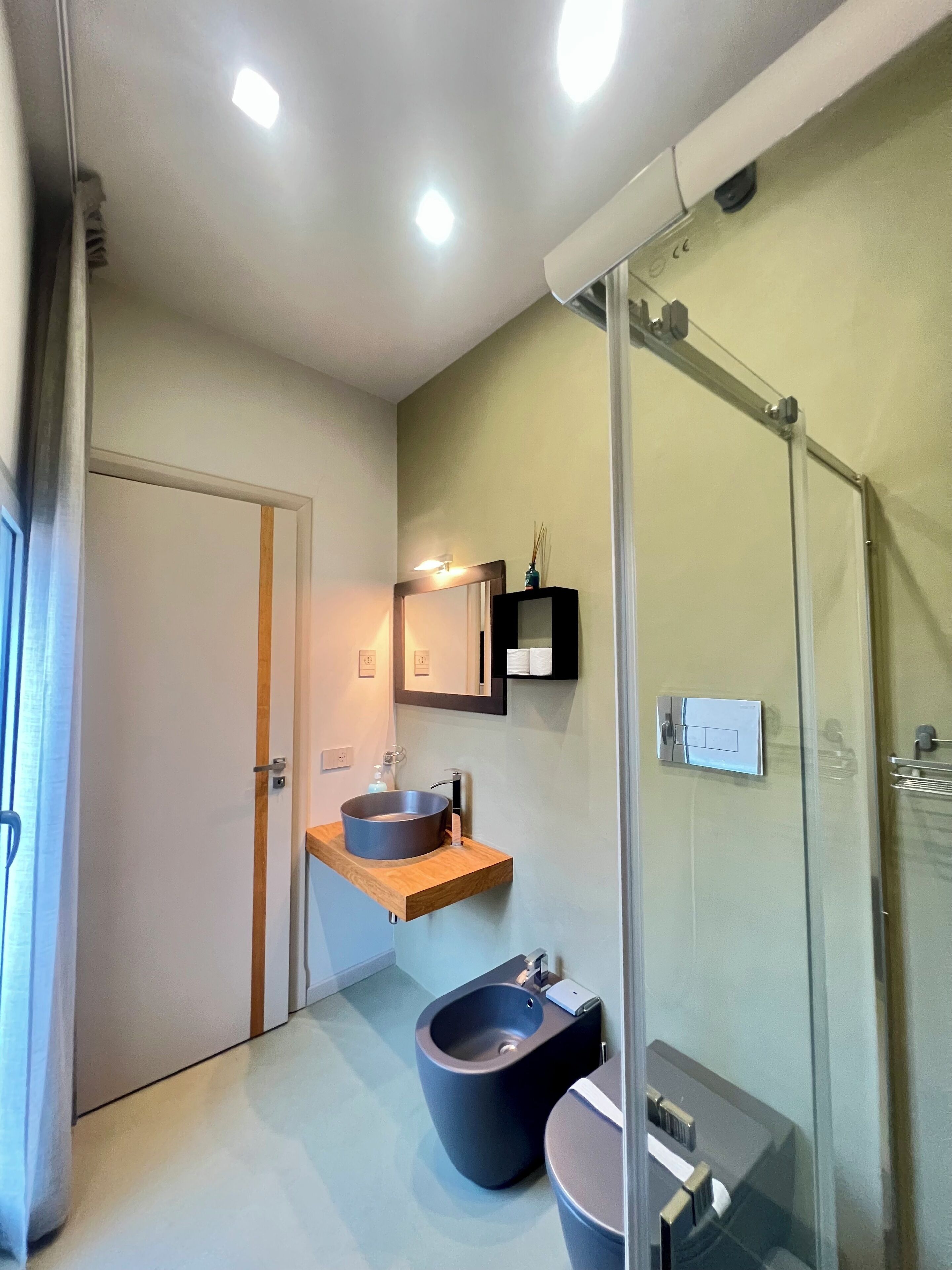 A modern bathroom with a glass shower enclosure, a wooden vanity with a round sink, and a bidet.