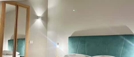 A bedroom with a large bed, a mirror, and a bedside table with a lamp.