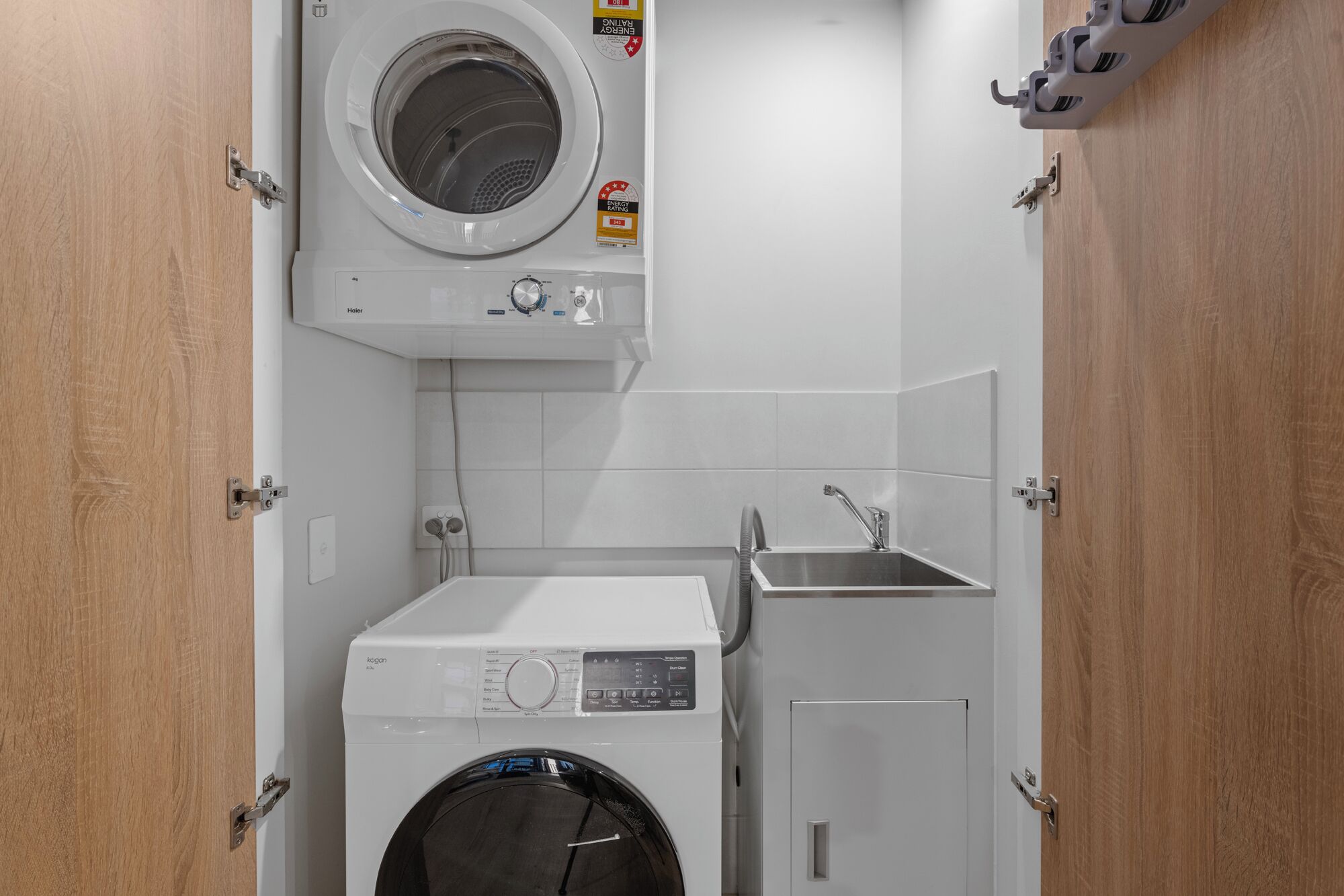 Une petite buanderie équipée d’un lave-linge et d’un sèche-linge à chargement frontal, d’un évier et d’un porte-serviettes.