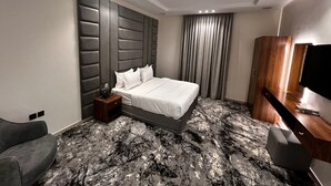 Ein modernes Hotelzimmer mit einem großen Bett, einem Schreibtisch, einem Sessel und einem Fernseher.