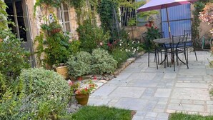 Un patio de piedra con una mesa y sillas, rodeado de abundante vegetación y plantas con flores.