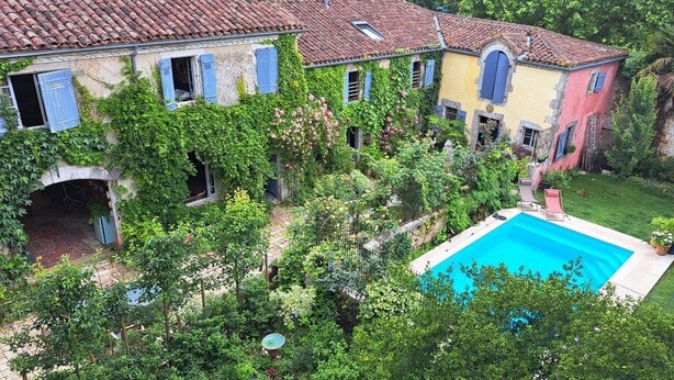 Un patio con piscina, rodeado de abundante vegetación y un edificio de varios pisos con contraventanas azules.
