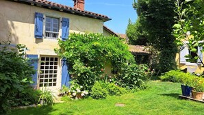 Una casa con jardín, una ventana con persianas azules y una puerta con panel de vidrio.
