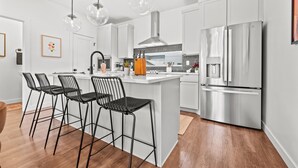 Una cocina moderna con armarios blancos, un refrigerador de acero inoxidable y una barra con taburetes negros.