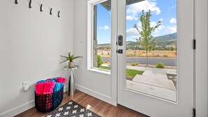 Una entrada moderna con una puerta de vidrio corredera, una mesita auxiliar con una planta en maceta y una cesta tejida de colores.