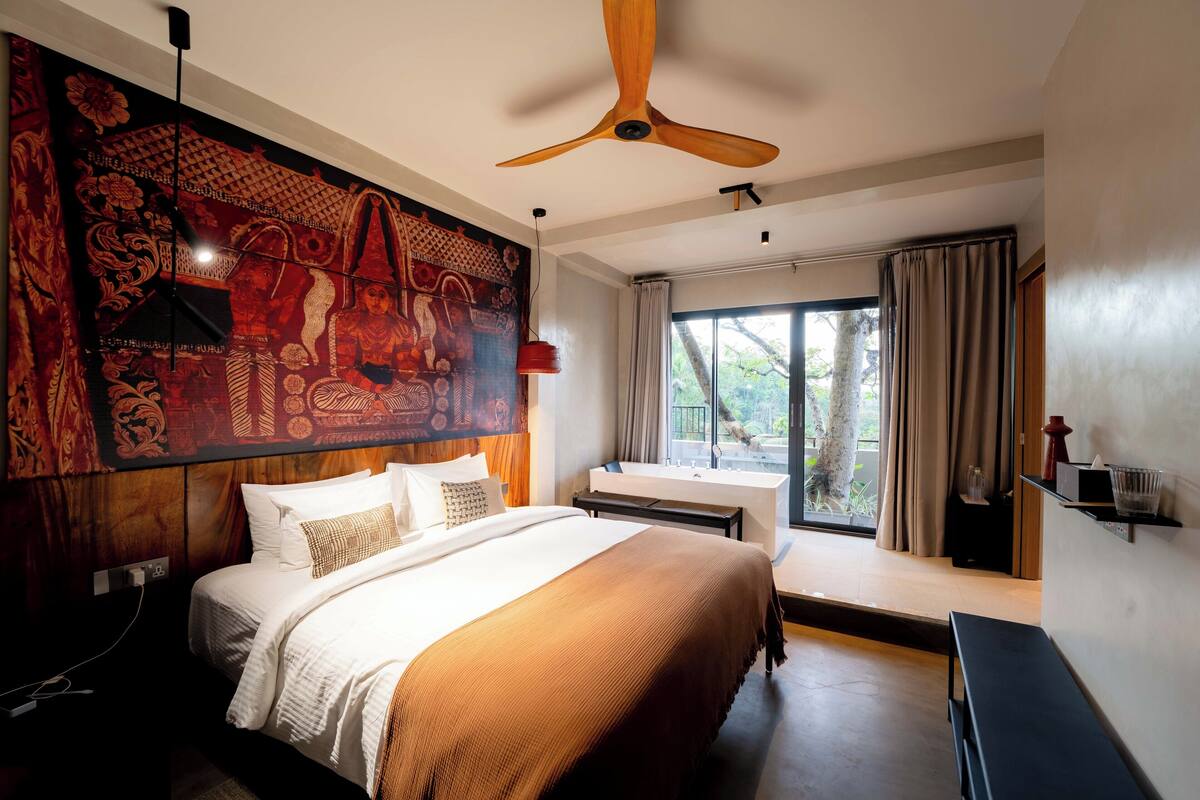 Une chambre d’hôtel moderne avec un grand lit, un ventilateur de plafond, une grande fenêtre avec des rideaux et une tapisserie murale.