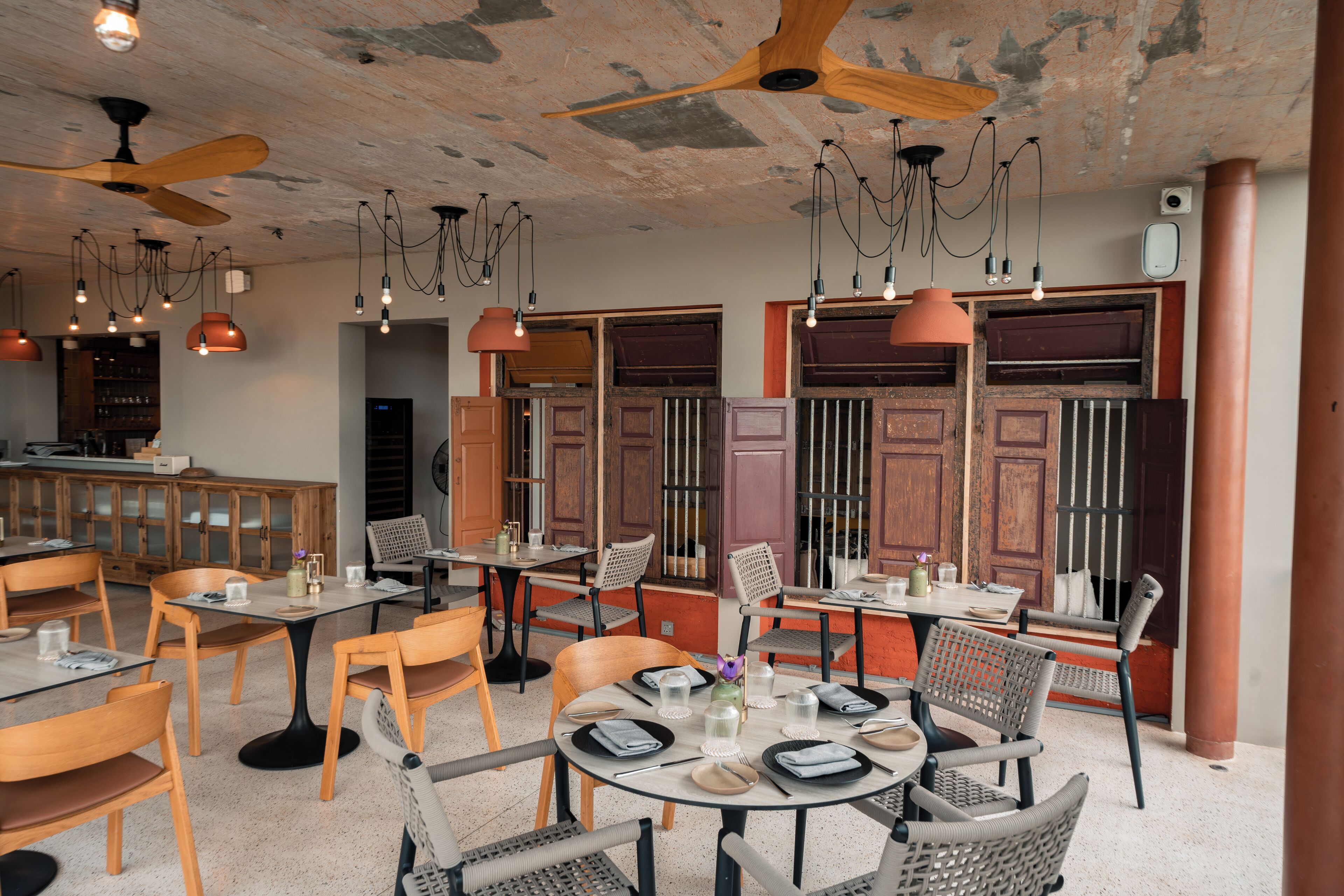 A restaurant interior with round tables, chairs, pendant lighting, and a ceiling fan.