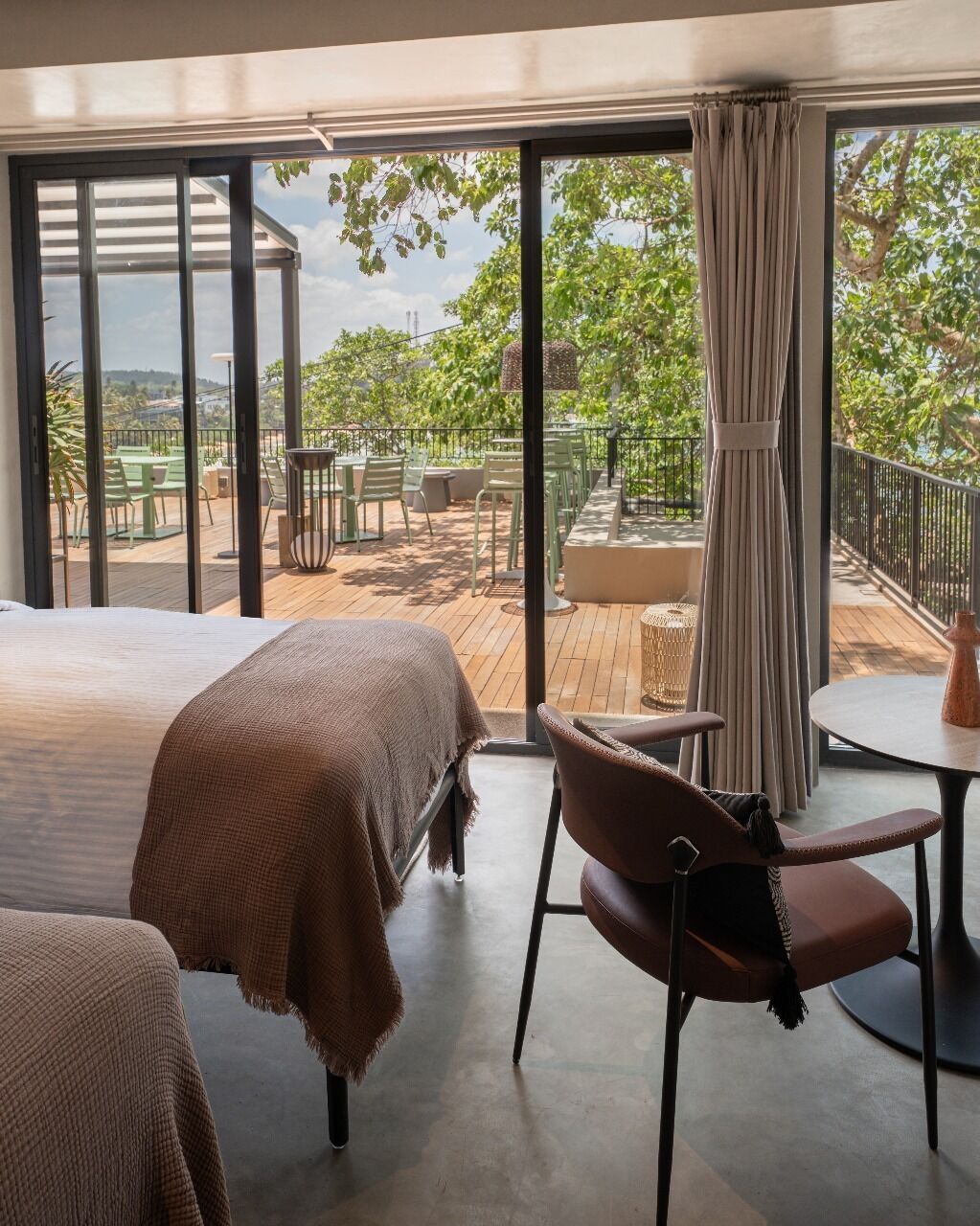 Habitación de hotel con una cama grande, una silla y vistas a un patio exterior con mesas y sillas.