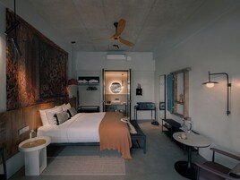 A modern hotel room with a large bed, a desk, a chair, a small table, a mirror, and a ceiling fan.