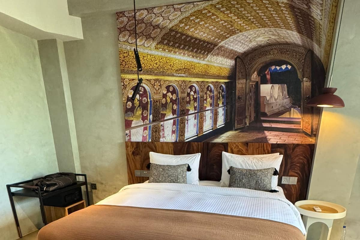 Une chambre moderne avec un grand lit, un banc, une table de chevet et une tapisserie murale.