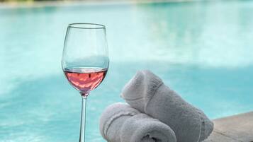 A glass of red wine and two rolled towels by a poolside.