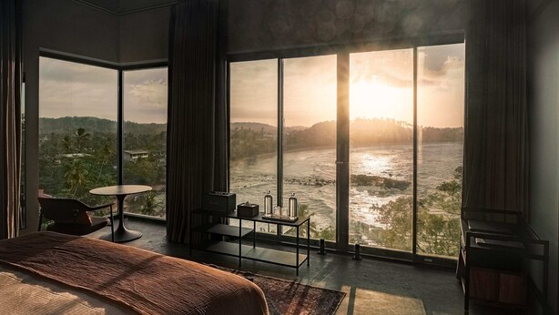 Un dormitorio espacioso con un gran ventanal con vistas a un río y colinas.