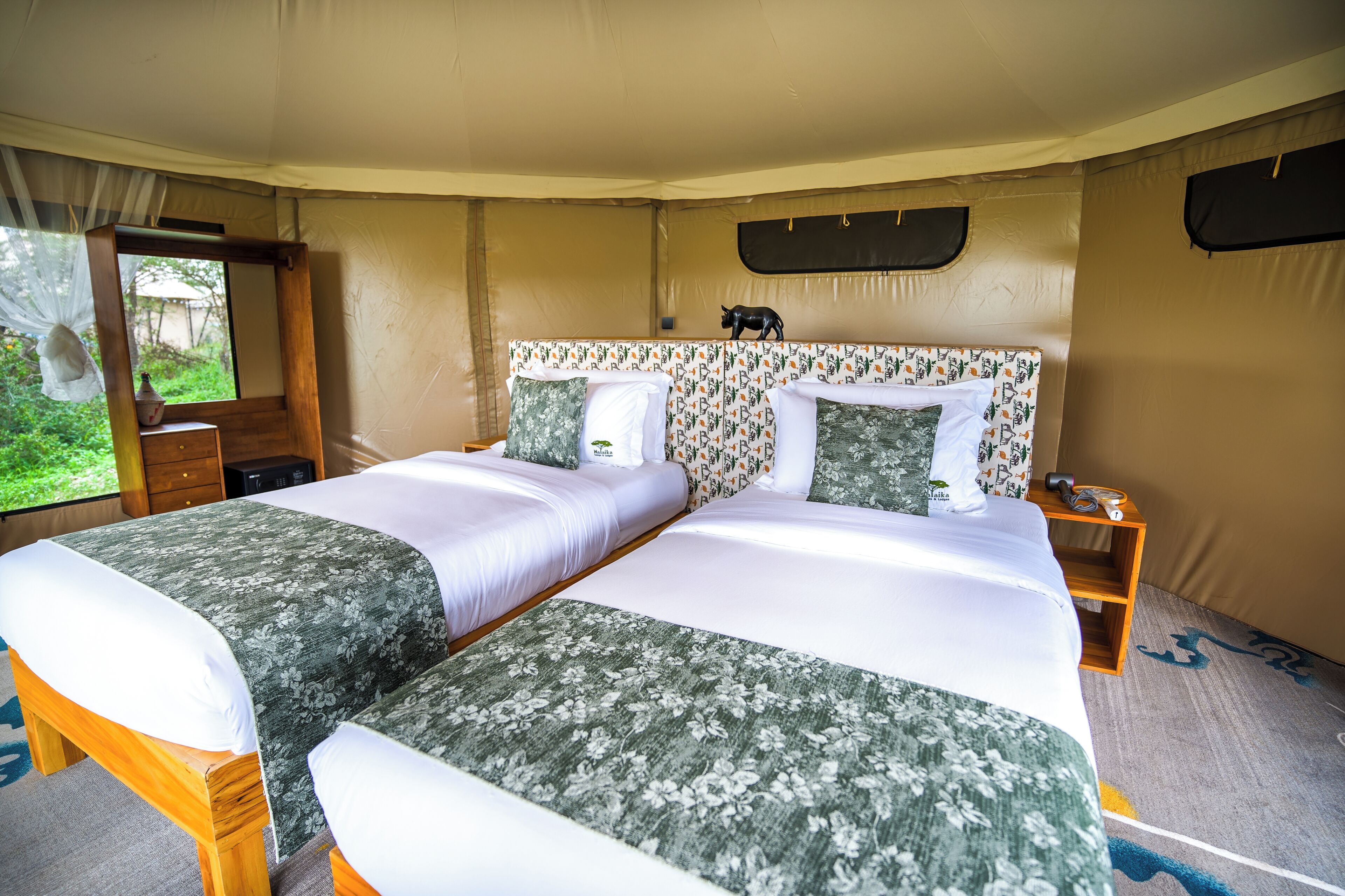 Una cama doble con ropa de cama floral, una mesita de noche con lámpara y una ventana con cortinas.