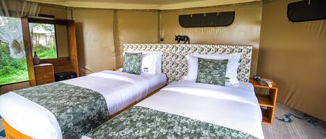 Una cama doble con ropa de cama floral, una mesita de noche con lámpara y una ventana con cortinas.