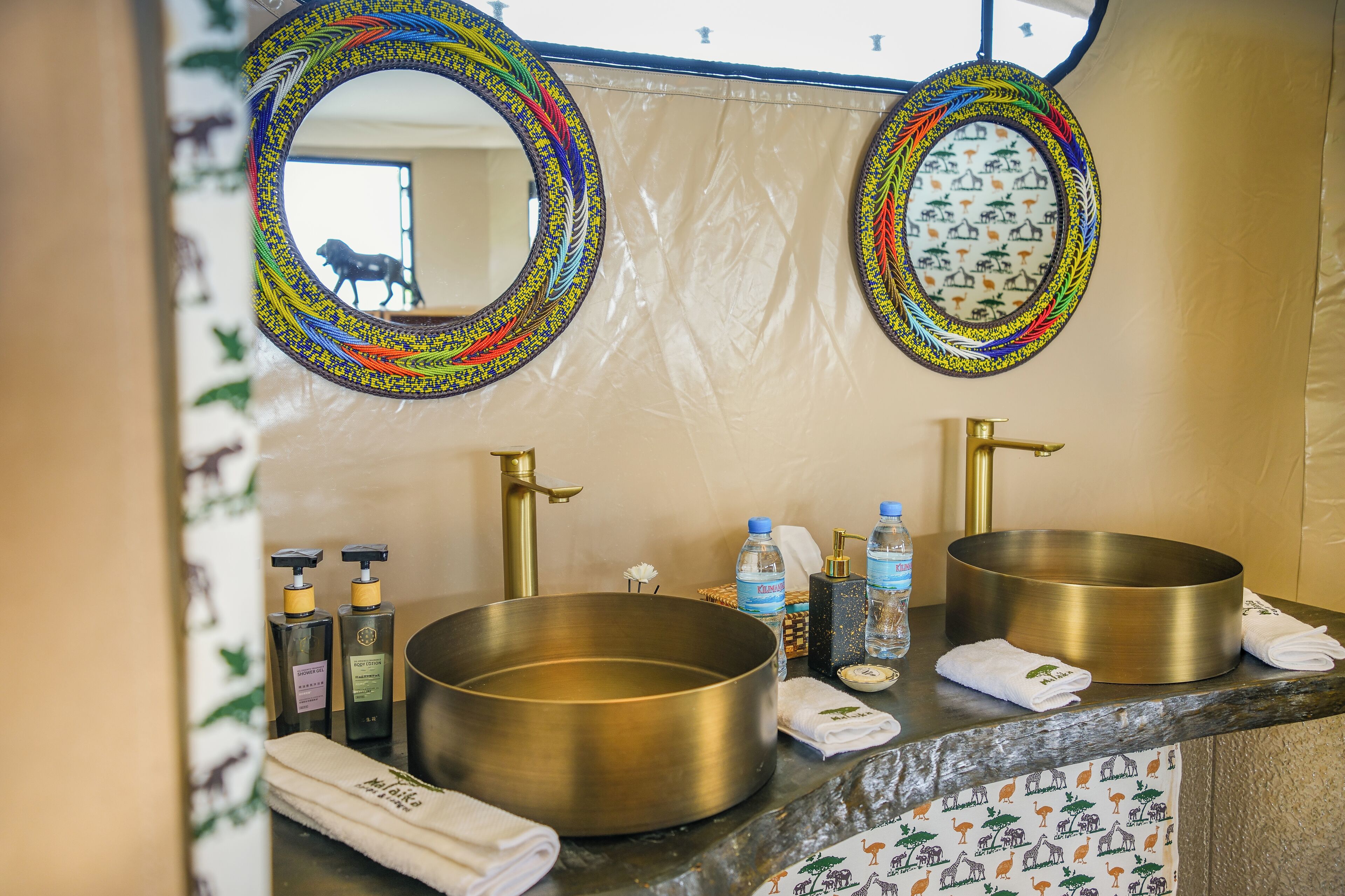 A bathroom with two large brass sinks, a mirror with a colorful frame, and toiletries on the counter.
