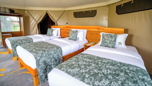 A tented room with two beds, a wooden headboard, and a small table. - Malaika Ndutu Luxury Camp (Ngorongoro)