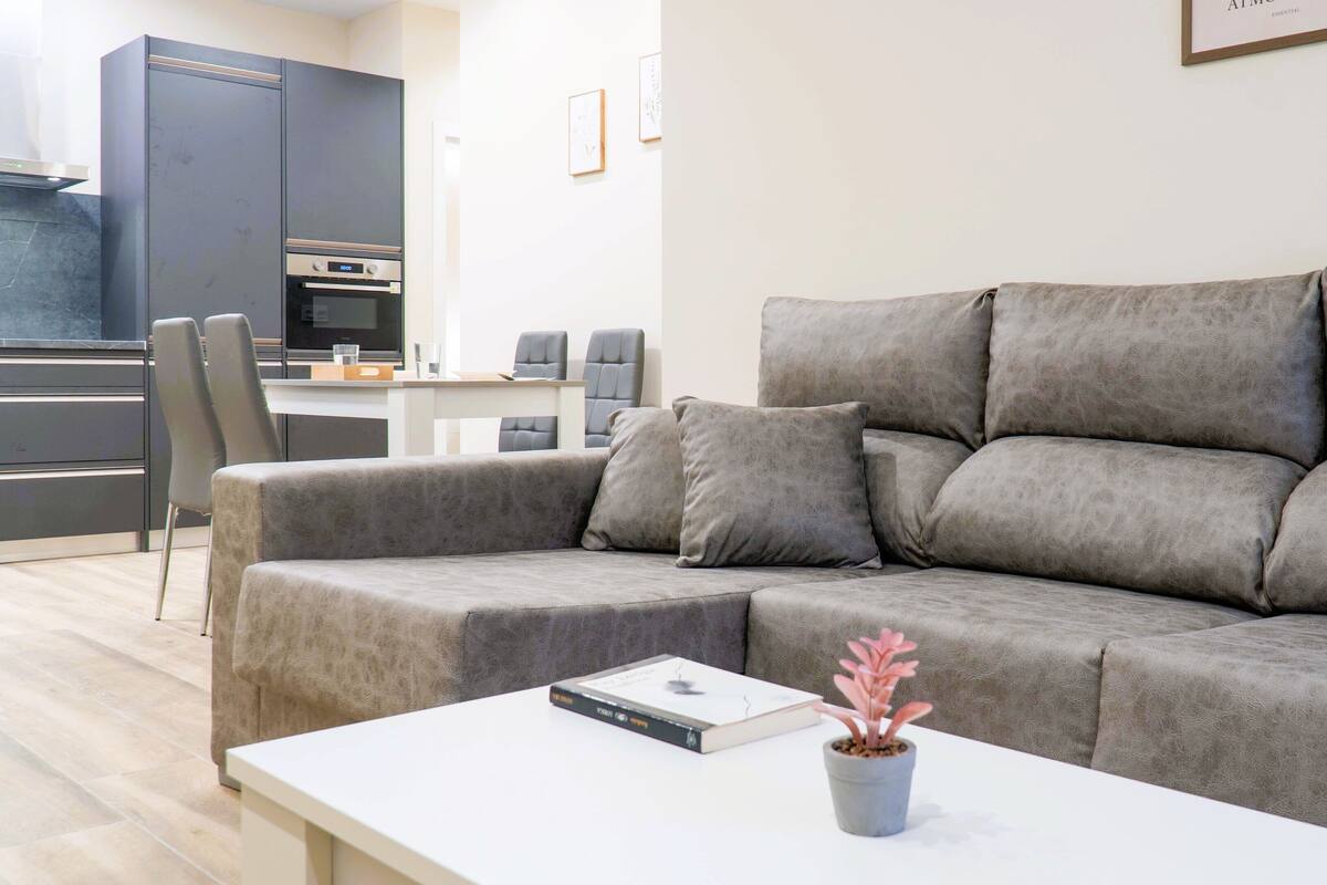 A modern living room with a grey sectional sofa, a white coffee table, and a potted plant.
