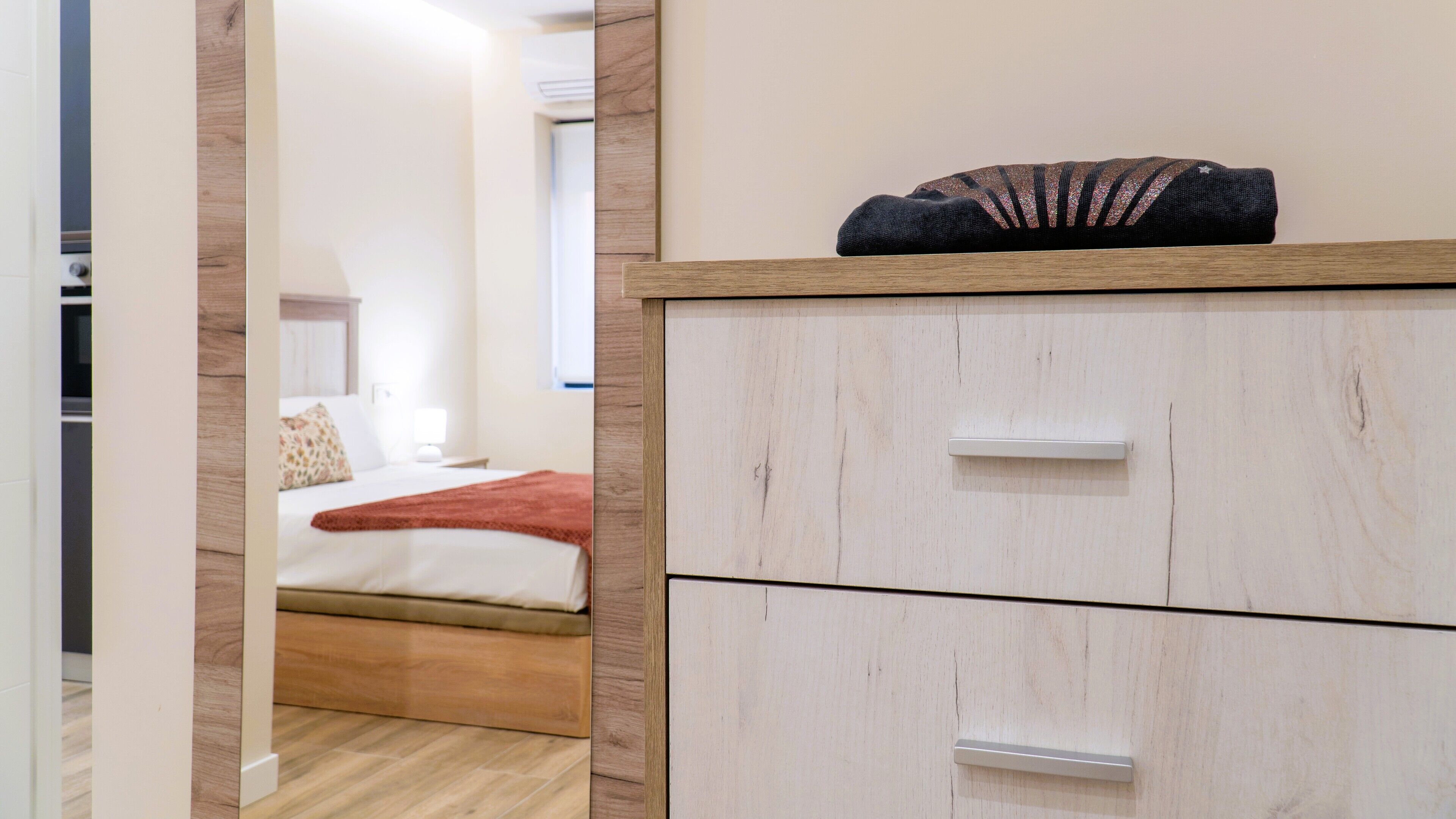 Un dormitorio moderno con una cama de madera, una mesita de noche blanca y un aparador de madera con cajones.