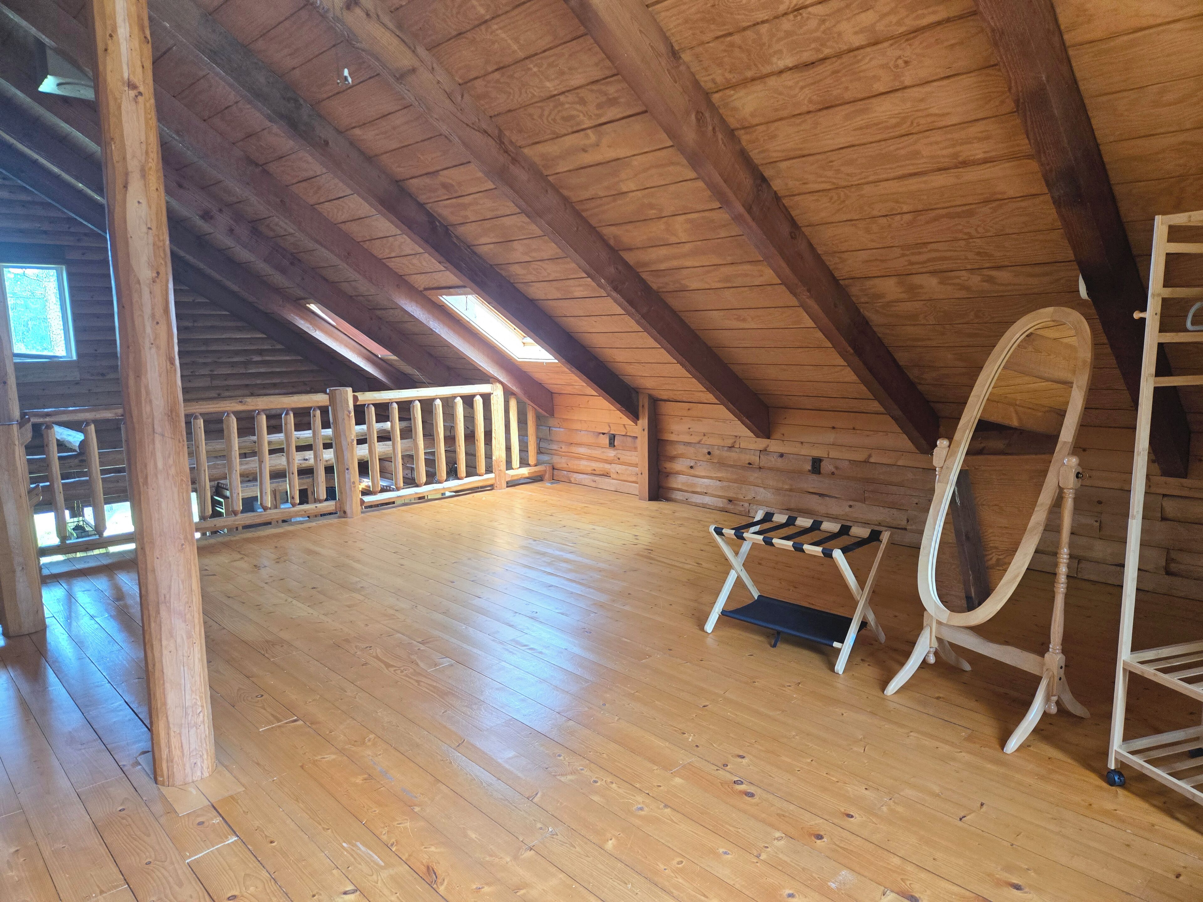 Un'ampia stanza mansardata con travi in legno, pavimento in legno, una piccola panca e una scala.