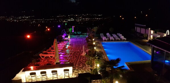 A nighttime view of a pool area with lounge chairs and a pool, surrounded by a stone pathway and illuminated by colorful lights. - hotel Labyrinth (Tbilisi)
