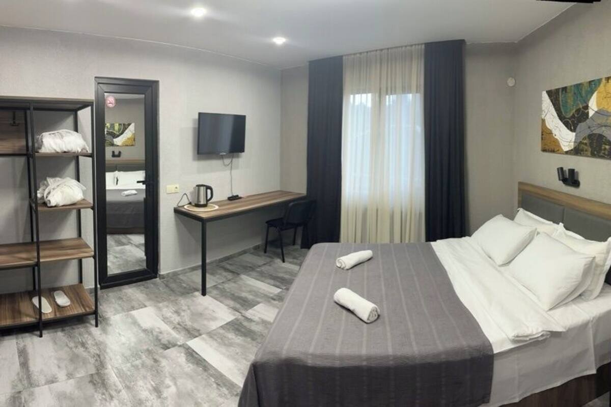 A hotel room with a bed, a desk, a chair, a wardrobe, and a fan.