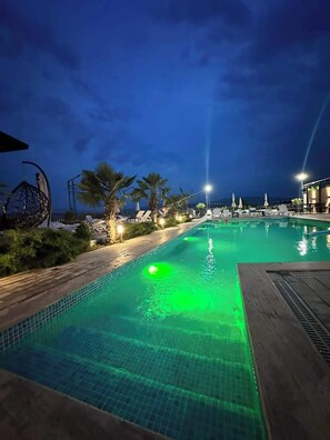 A nighttime pool area with a green light, palm trees, and lounge chairs. - hotel Labyrinth (Tbilisi)