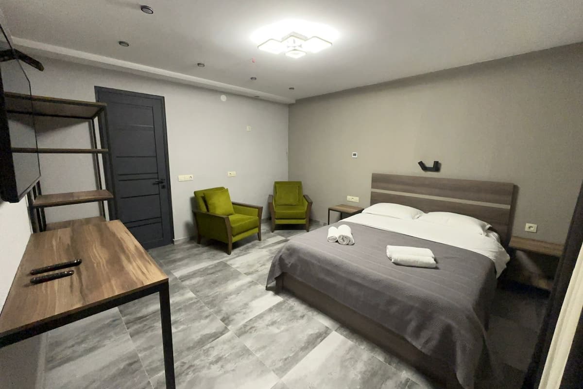 A hotel room with a bed, two chairs, a small table, and a TV on the wall.