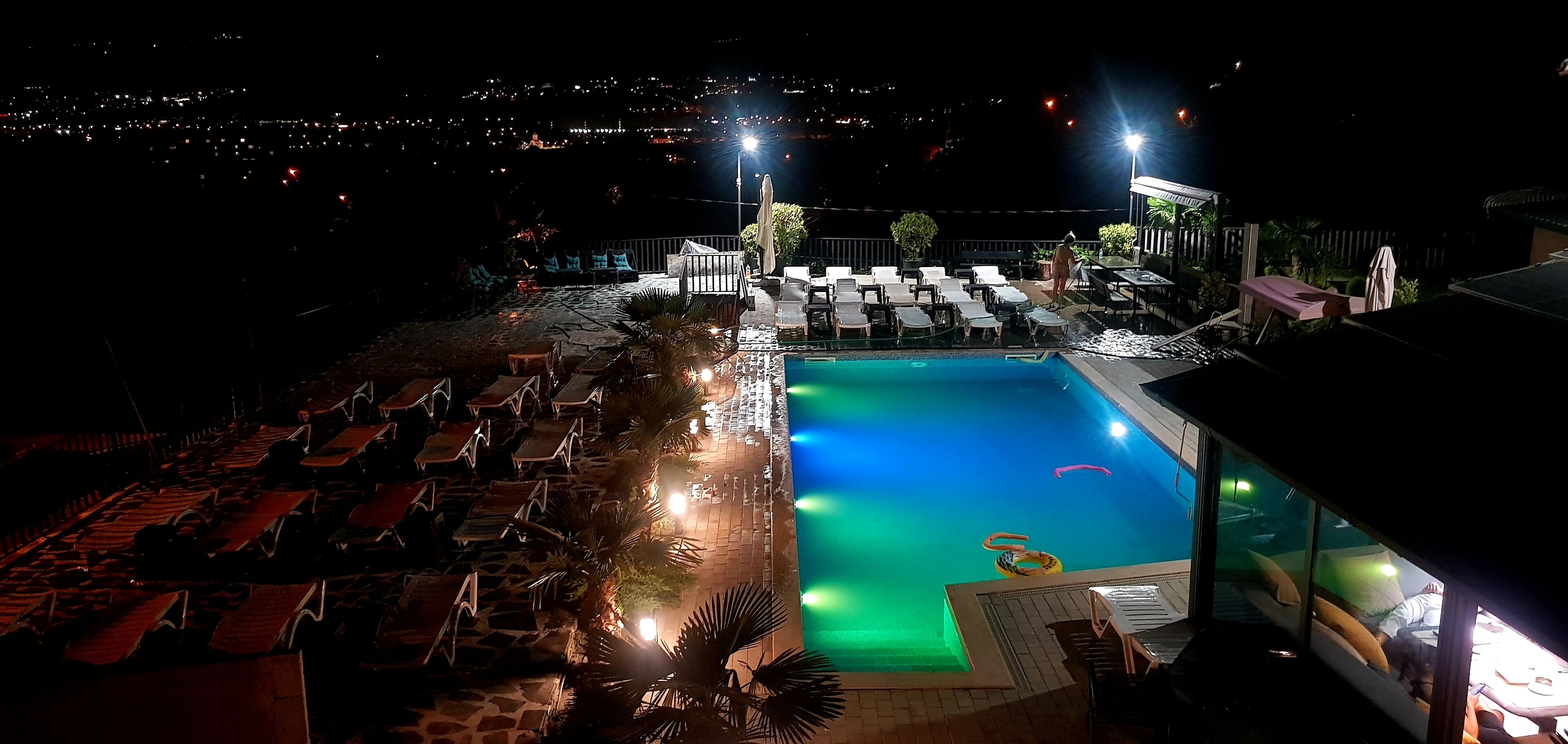 A nighttime view of a hotel pool area with lounge chairs and a swimming pool.
