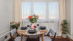 En matplats med ett runt bord dukat för fyra personer, en vas med blommor och en krukväxt.