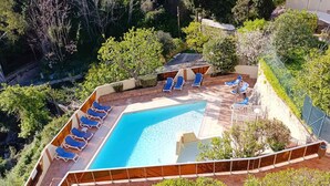 Una piscina con sillas reclinables azules, rodeada de follaje y una zona vallada.