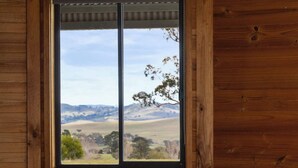 Interior de una cabaña de madera con un ventanal grande que ofrece vistas a un paisaje montañoso.